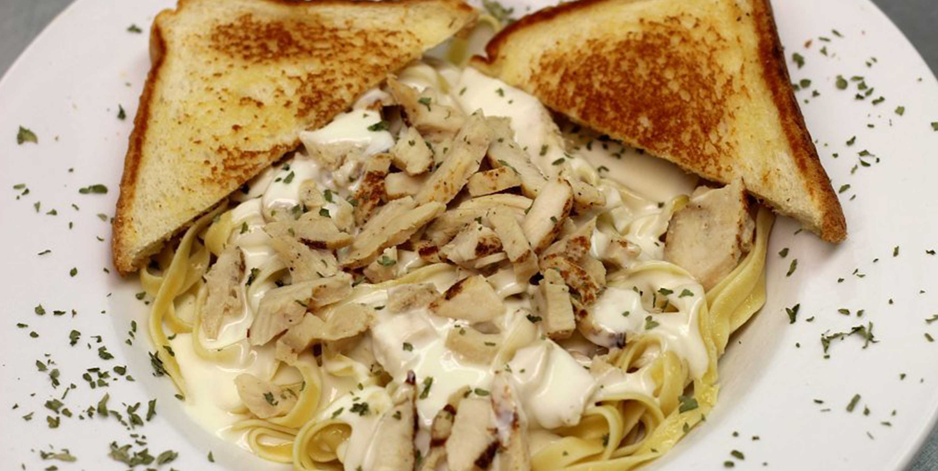 Grilled chicken alfredo pasta with golden slices of toast made at Main Gate Bar & Grill